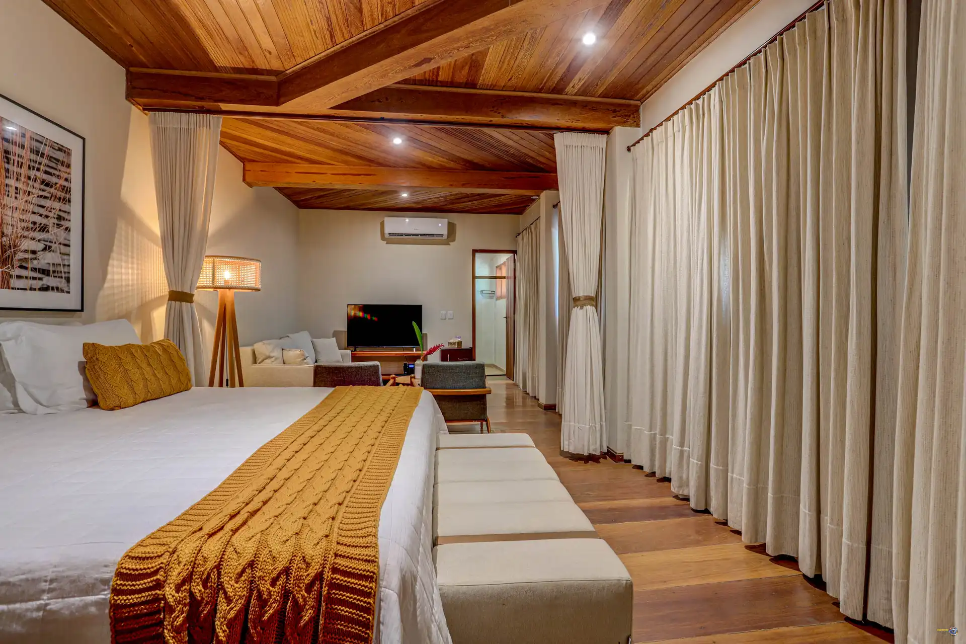 A cama queen size da Grand Cru em primeiro plano e a sala ao fundo