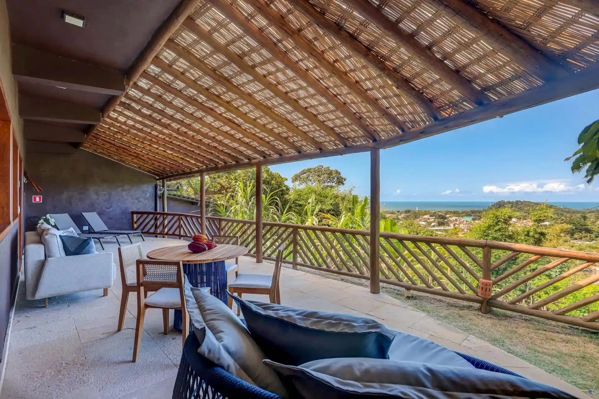 A varanda da Grand Cru sob o pergolado, com a mesa, o sofá e a costa ao fundo