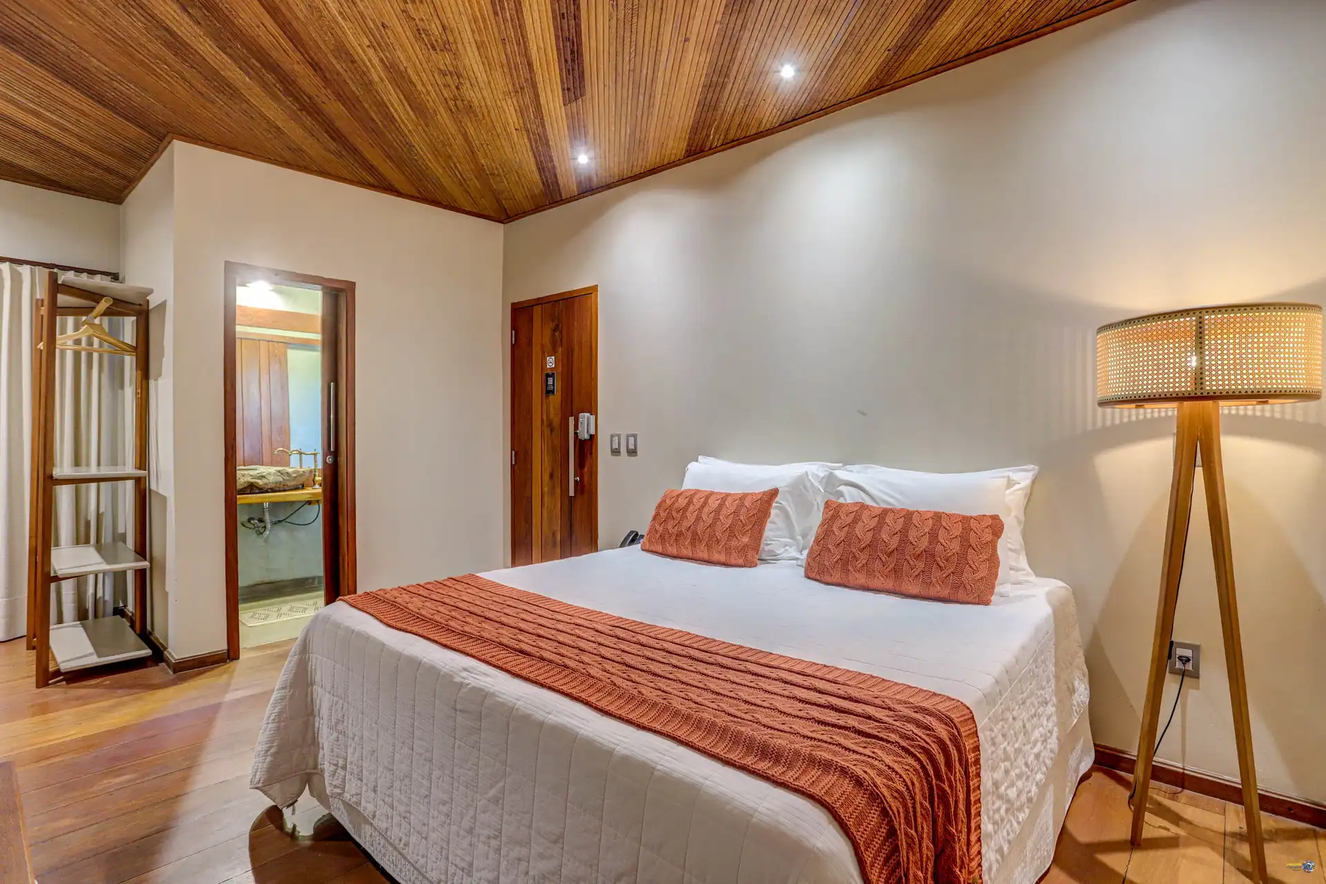 A cama queen size de uma suíte Semente, com a luminária de palha e o forro de madeira