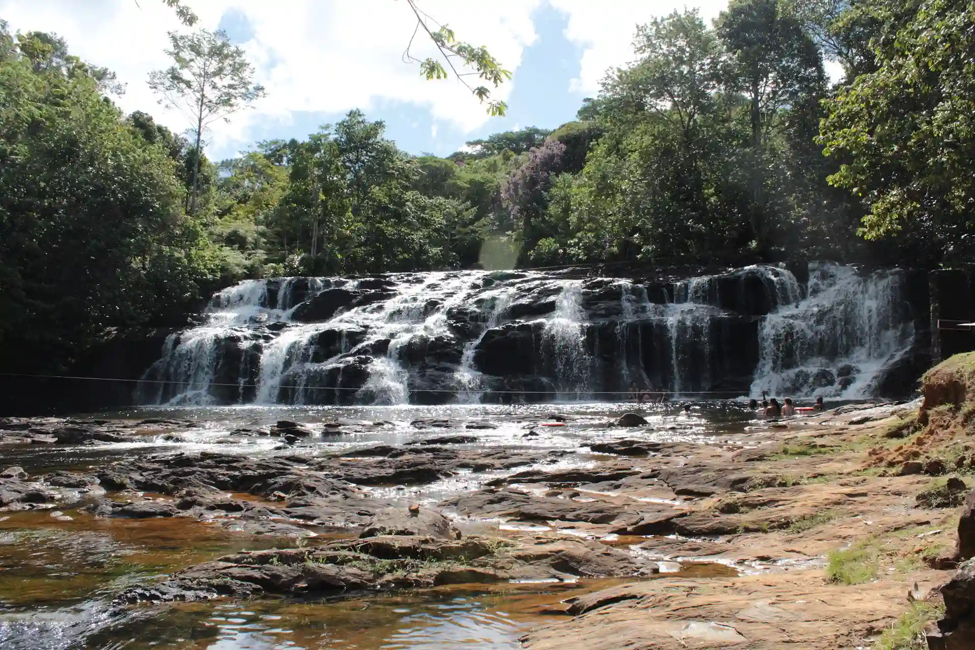 A Cachoeira do Tijuípe: uma queda larga e baixa sobre pedras escuras, com a mata em volta