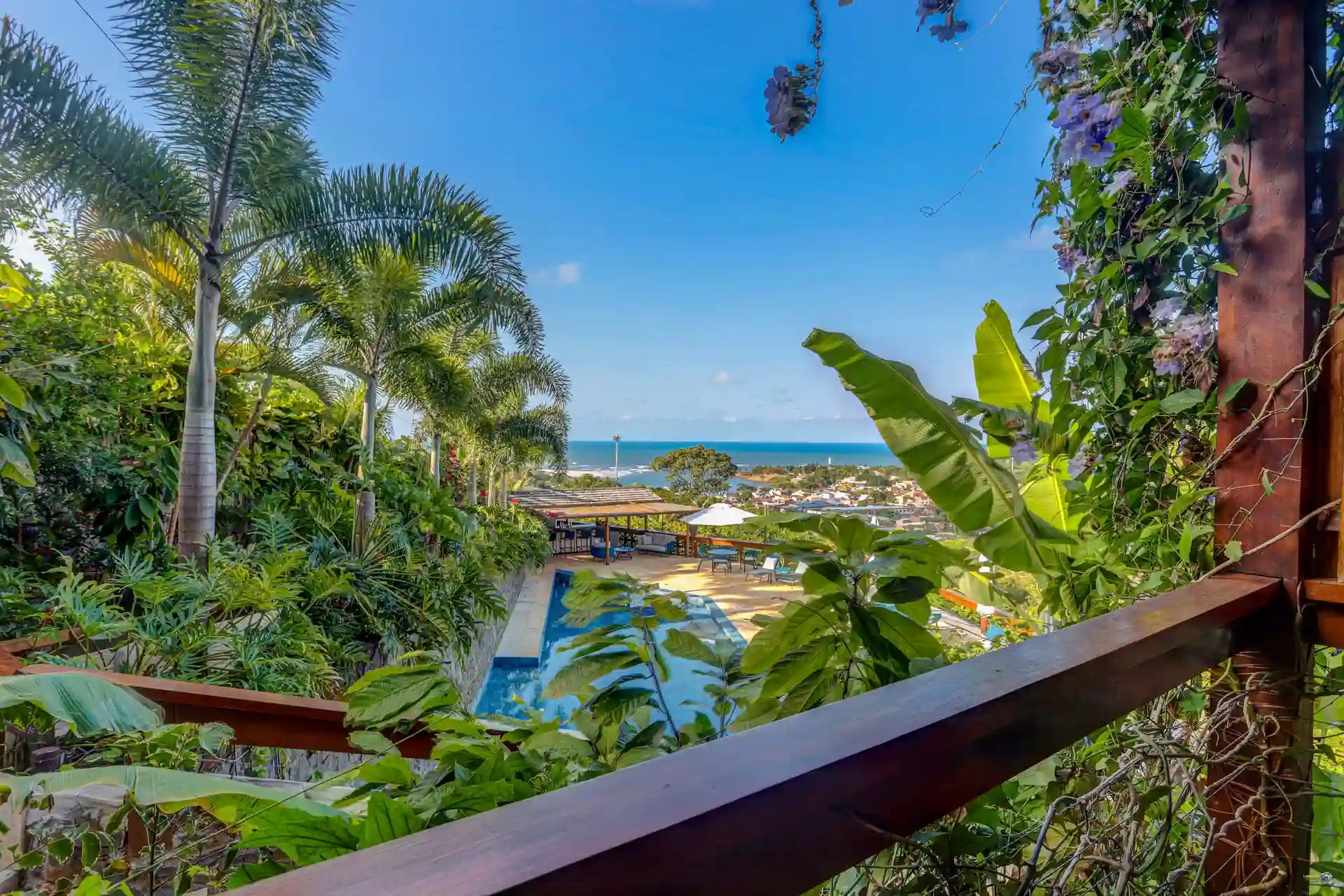 A varanda de uma suíte Torra entre coqueiros e bananeiras, com a piscina embaixo e o mar no fundo